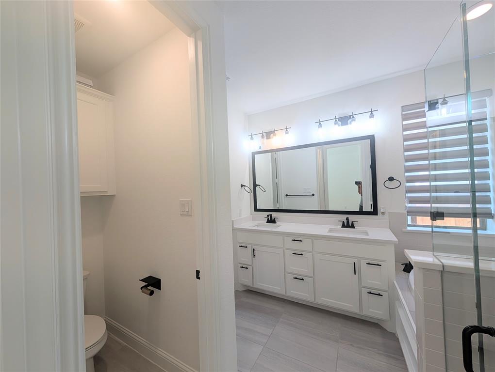 15532 Fringe Tree Road Frisco, TX 75035 - Photo 9 of 31 Contemporary bathroom with dual white vanity, white countertops, black hardware, glass-enclosed shower, and separate commode room with built-in cabinetry