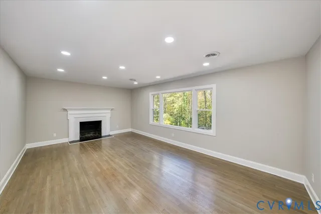 an empty room with wooden floor fireplace and windows