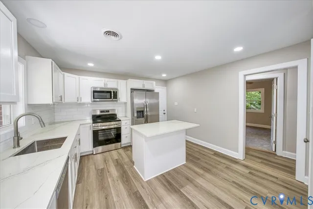 a kitchen with stainless steel appliances a stove a sink a refrigerator white cabinets and wooden floor