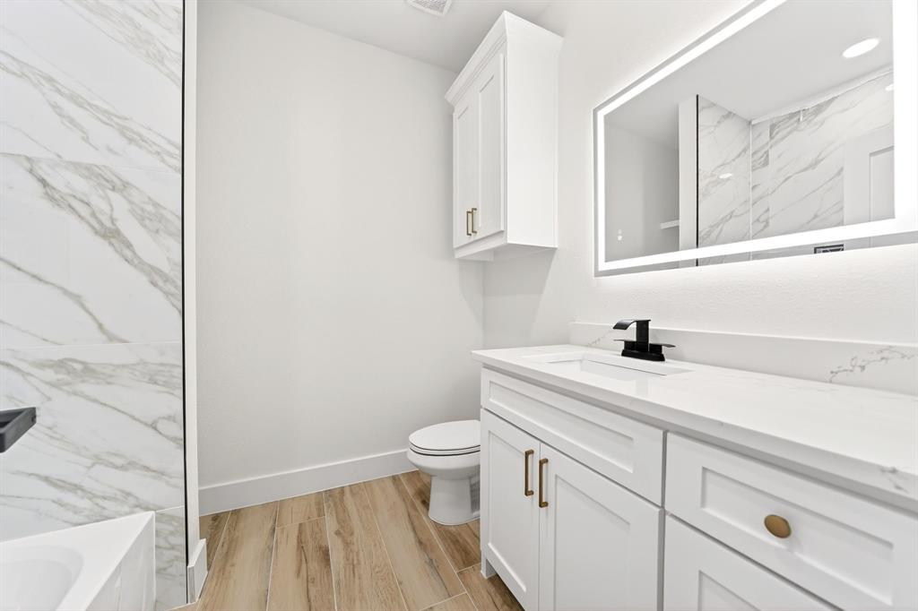 120 Springwood Road Enchanted Oaks, TX 75156 - Photo 31 of 37 Vanity area featuring an illuminated mirror, white shaker-style cabinetry with gold-tone hardware, and a white countertop with integrated sink