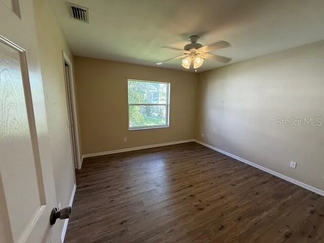 a view of an empty room with wooden floor and a ceiling fan