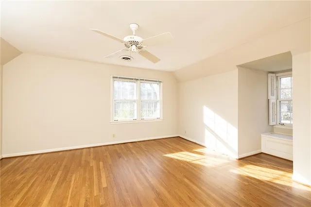 an empty room with wooden floor chandelier fan and windows
