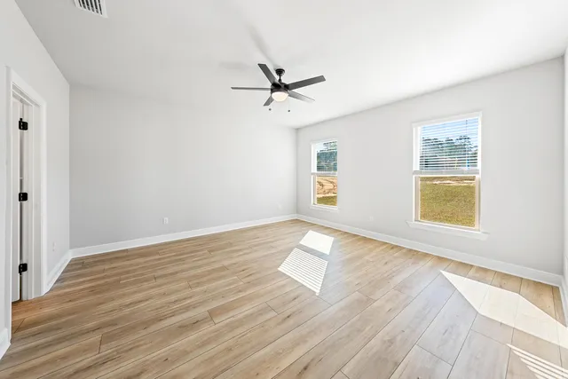 an empty room with wooden floor ceiling fan and windows
