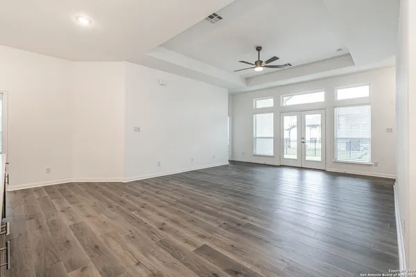 a view of an empty room with wooden floor and a ceiling fan