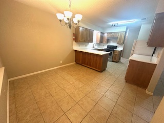 102 Verna Spur, Unit A Georgetown, TX 78628 - Photo 17 of 20 Kitchen with light countertops, a peninsula, a chandelier, pendant lighting, and brown cabinets