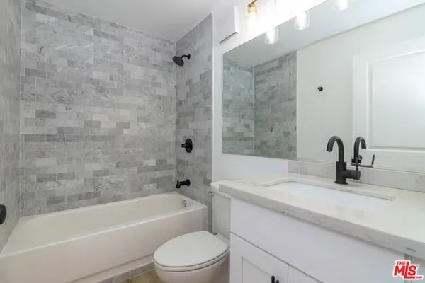 a bathroom with a granite countertop bathtub shower sink vanity and toilet