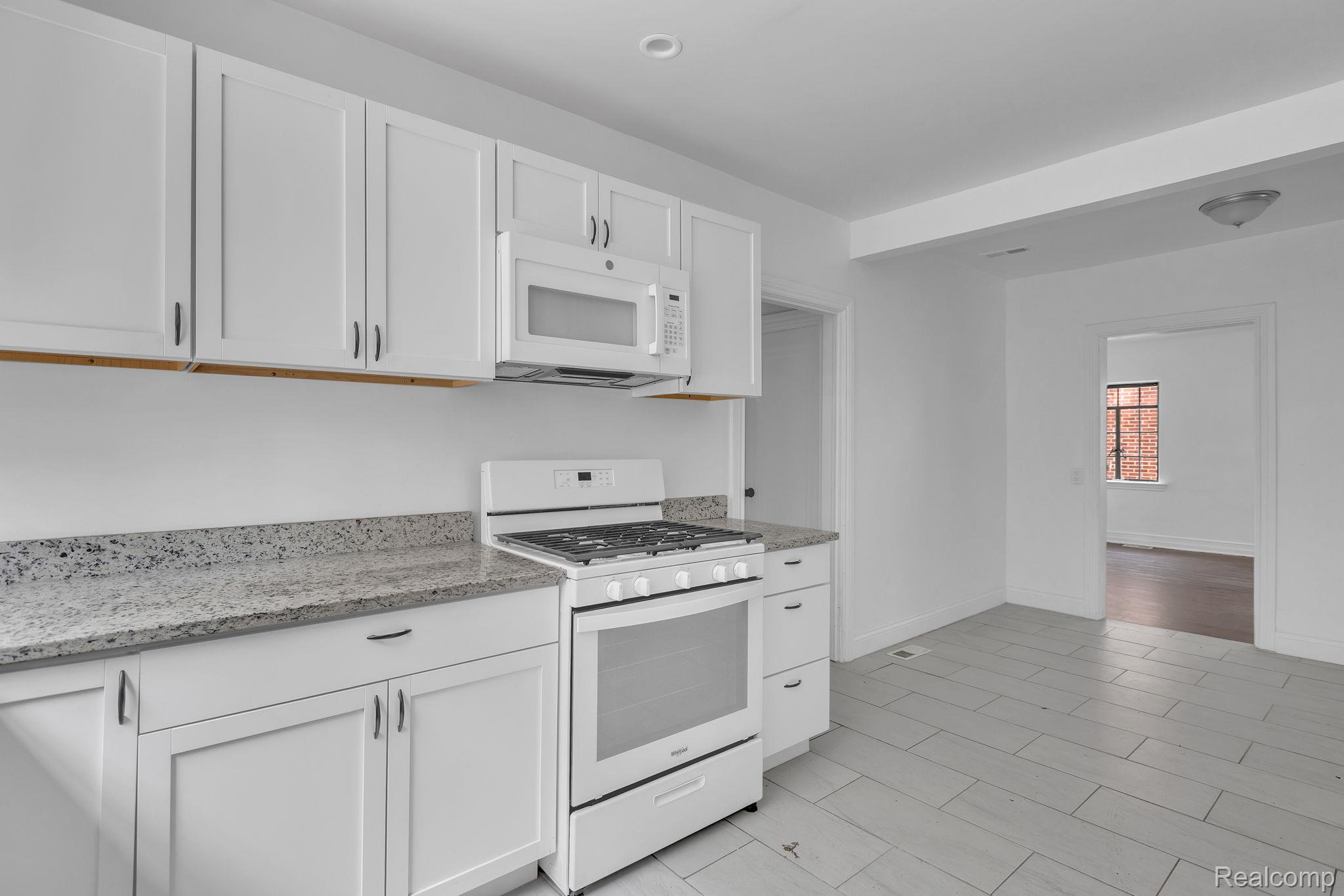 19510 Stratford Road Detroit, MI 48221 - Photo 22 of 45 Kitchen featuring white cabinetry, speckled countertops, a white range with an overhead microwave, and light grey tile flooring