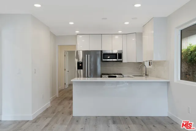 a kitchen with stainless steel appliances a sink a stove a refrigerator cabinets and a window