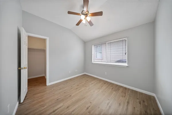 an empty room with wooden floor chandelier fan and windows