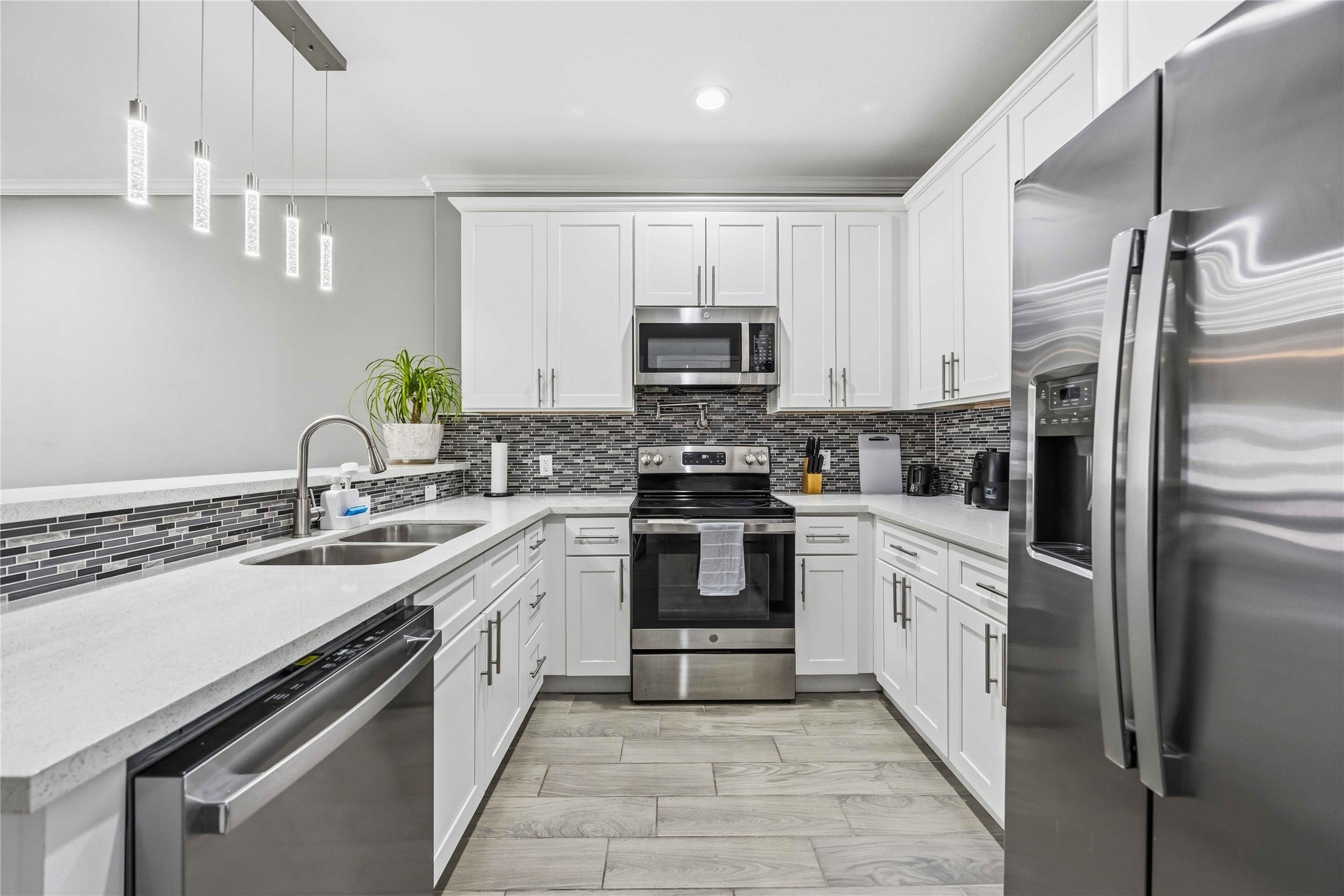 4903 Mallow Street, Unit A Houston, TX 77033 - Photo 6 of 10 All appliances are stainless steel, including a large French-door refrigerator, a slide-in electric range, a built-in microwave, and a double-basin undermount sink with a gooseneck faucet. The surfaces are a white quartz or granite with very subtle light gray veining, providing a crisp look against the white cabinets.