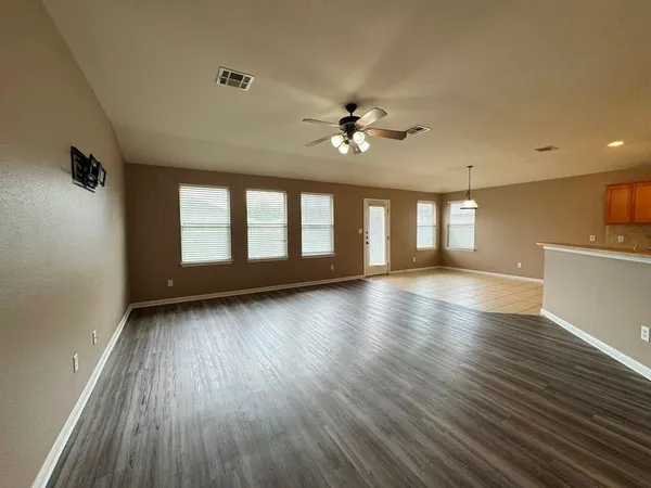 a view of an empty room with wooden floor and a kitchen