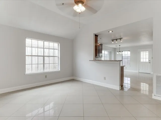 an empty room with chandelier fan and windows