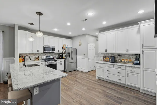 a kitchen with stainless steel appliances kitchen island granite countertop a stove a sink a refrigerator and white cabinets with wooden floor