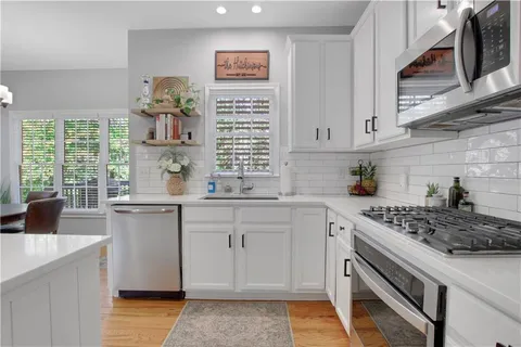 a kitchen with stainless steel appliances white cabinets a stove a sink a window and wooden floor