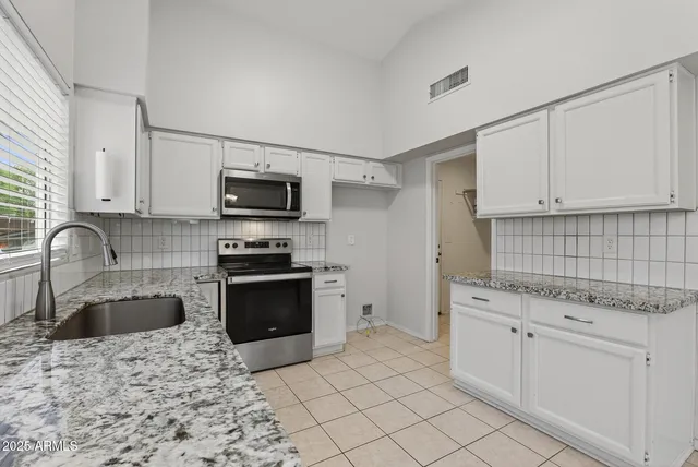 a kitchen with granite countertop a sink and a stove top oven with white cabinets