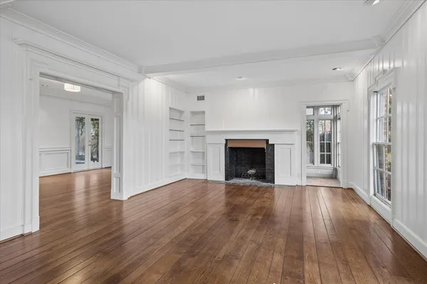 an empty room with wooden floor fireplace and windows