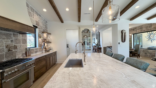 168 South Rancho Santa Fe Virgin, UT 84779 - Photo 16 of 58 Gourmet kitchen featuring a large stone accent wall, wood-beam ceiling, spacious island with integrated sink, stainless steel professional-grade range, and built-in wood cabinetry