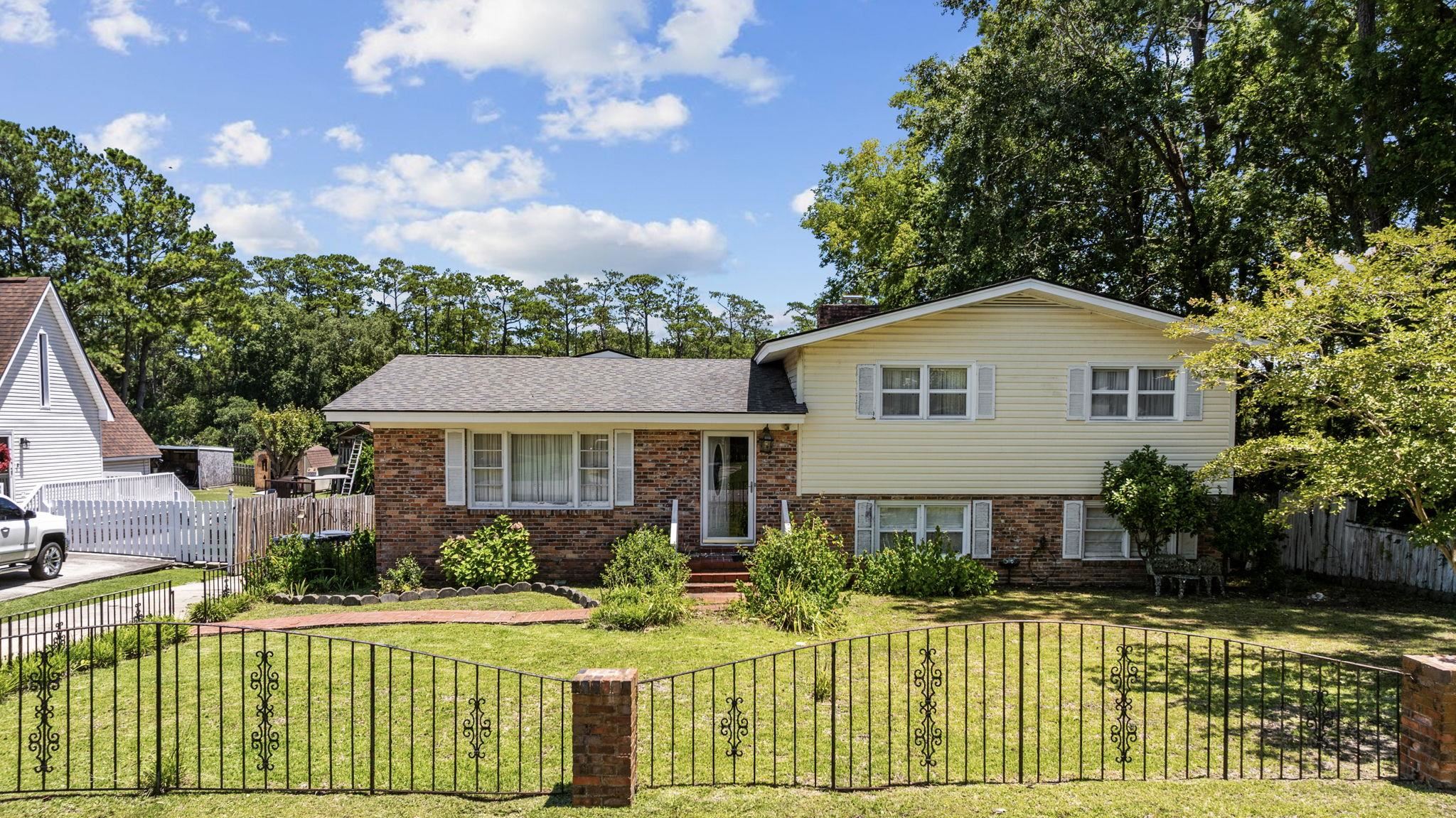Tri-level home with a fenced front yard, brick siding, a shingled roof, and a chimney