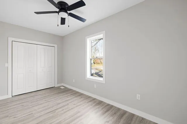 an empty room with wooden floor ceiling fan and windows