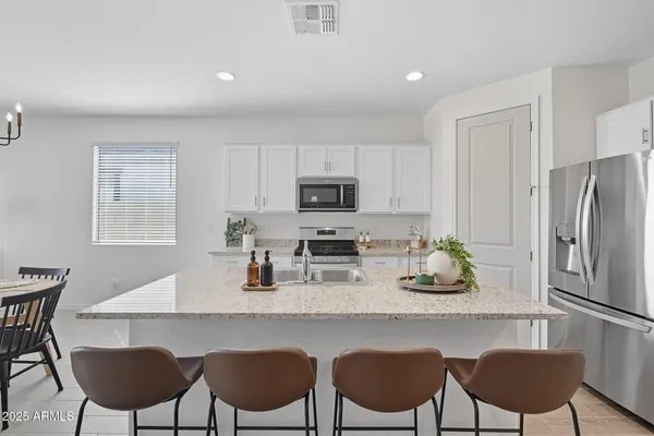 a kitchen with stainless steel appliances granite countertop a dining table chairs refrigerator and microwave