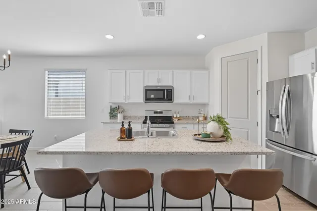 a kitchen with stainless steel appliances granite countertop a dining table chairs refrigerator and microwave