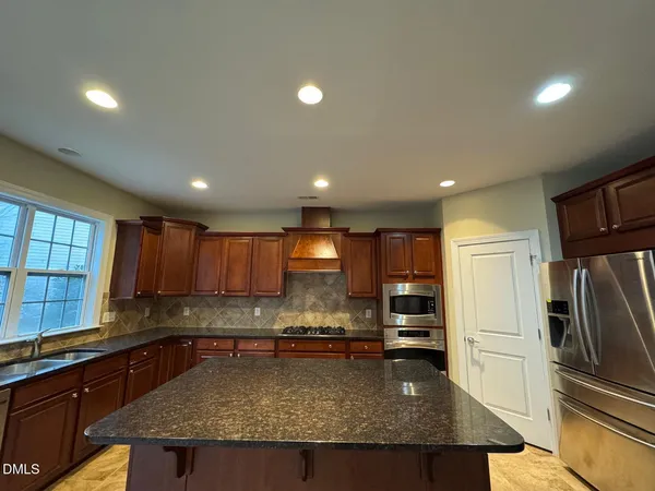a kitchen with kitchen island granite countertop a refrigerator a sink a stove a microwave a counter top oven and cabinets