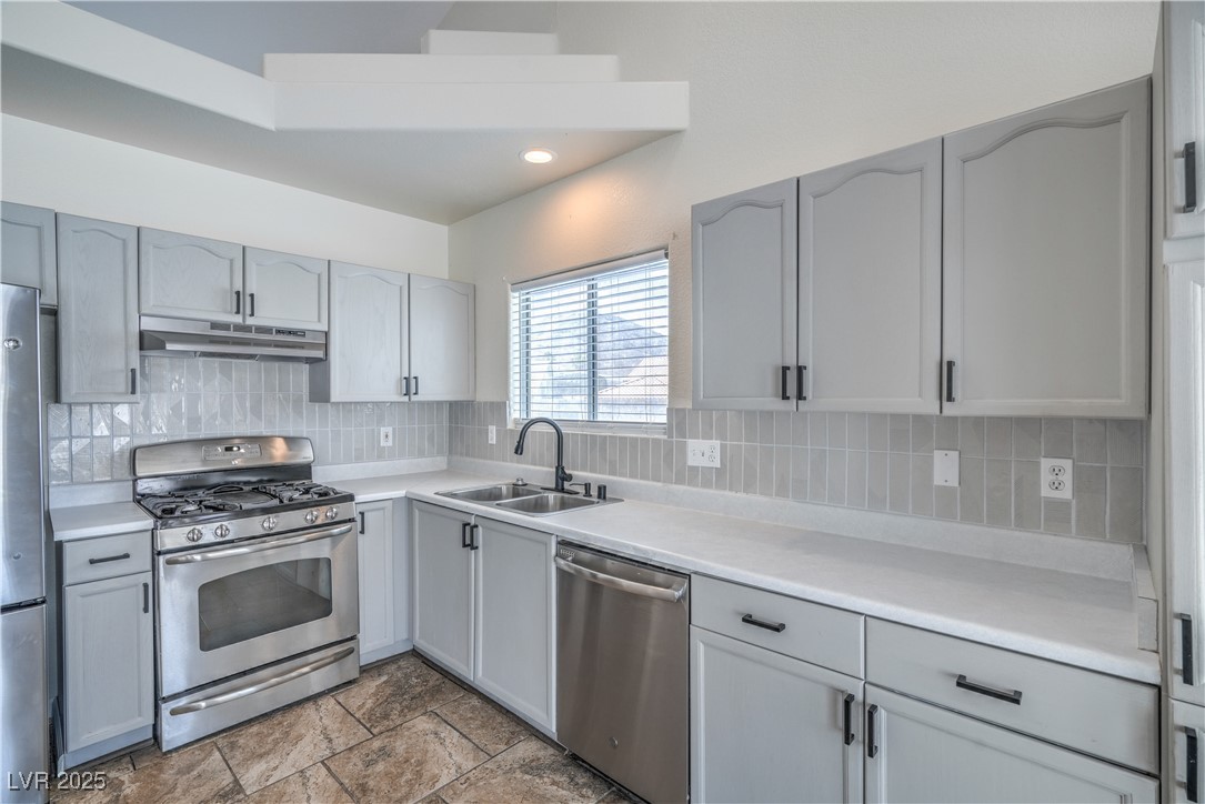 818 Coastal Beach Road Henderson, NV 89002 - Photo 16 of 39 Kitchen with stainless steel appliances, light countertops, decorative backsplash, under cabinet range hood, and gray cabinetry