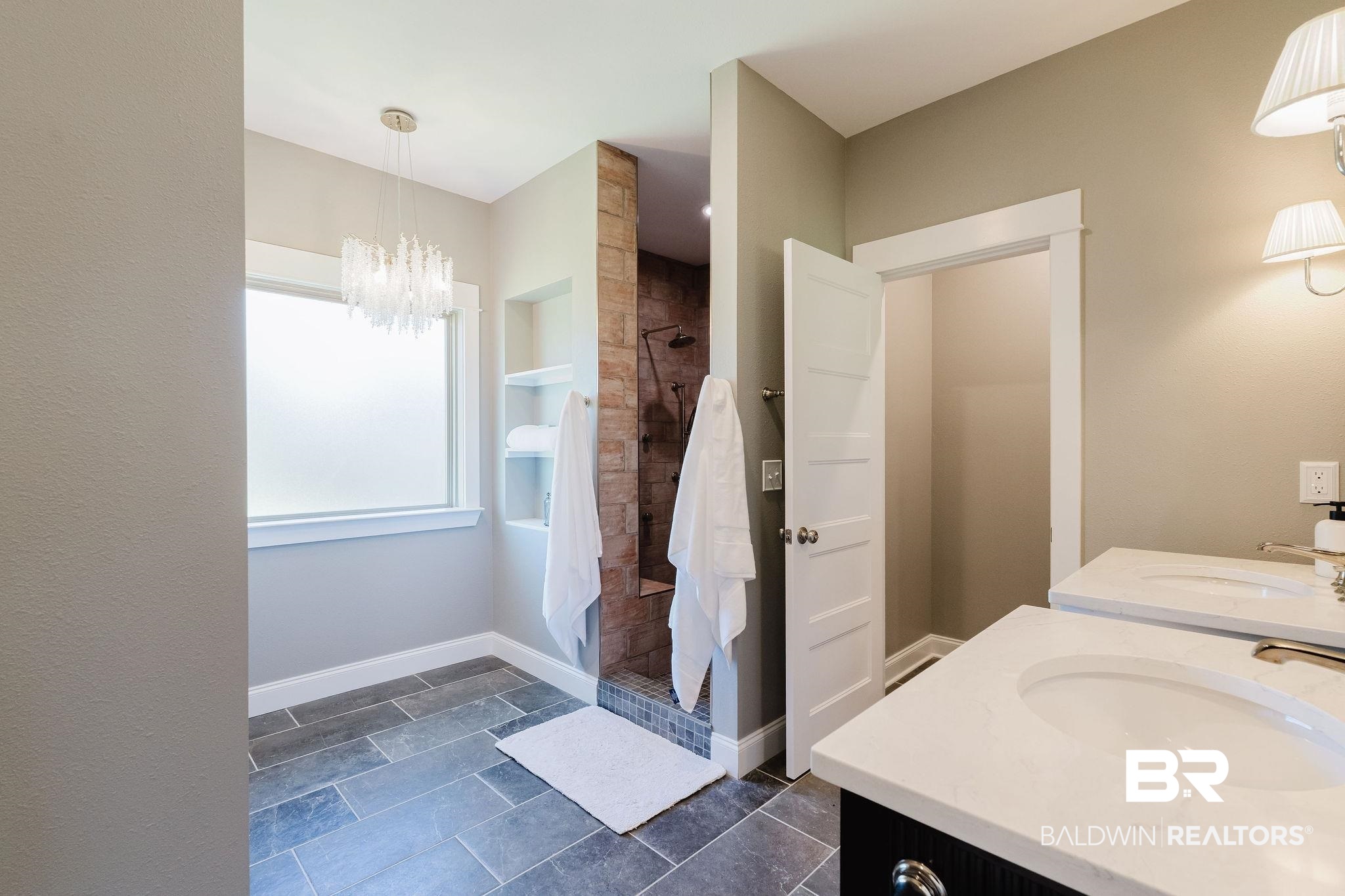 7872 Calverton Street Foley, AL 36535 - Photo 17 of 76 Bathroom featuring dual vanity with undermount sinks and white countertops, contrasting dark cabinetry, gray wall sconces, walk-in shower with stone-tile surround, and tiled flooring