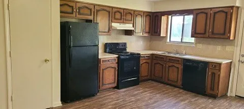 a kitchen with stainless steel appliances granite countertop a refrigerator a sink dishwasher a stove and a dining table with wooden floor