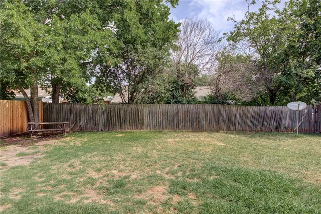 a view of a backyard with a fence and a large tree
