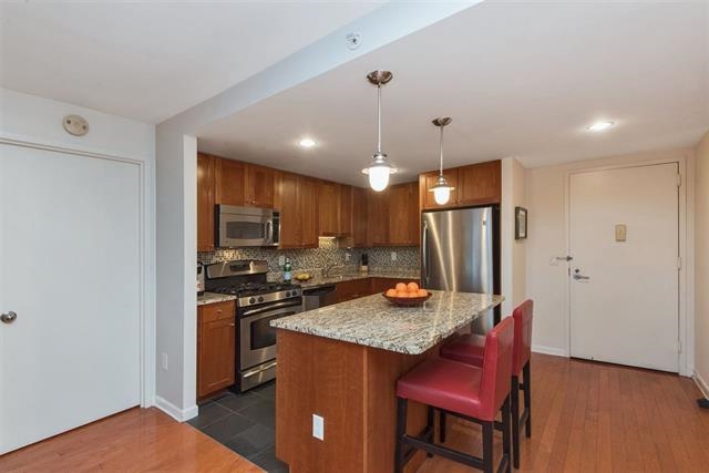 700 Grove Street, Unit 8R Jersey City, NJ 07310 - Photo 3 of 11 a kitchen with stainless steel appliances granite countertop a refrigerator a stove a sink dishwasher with a dining table and chairs