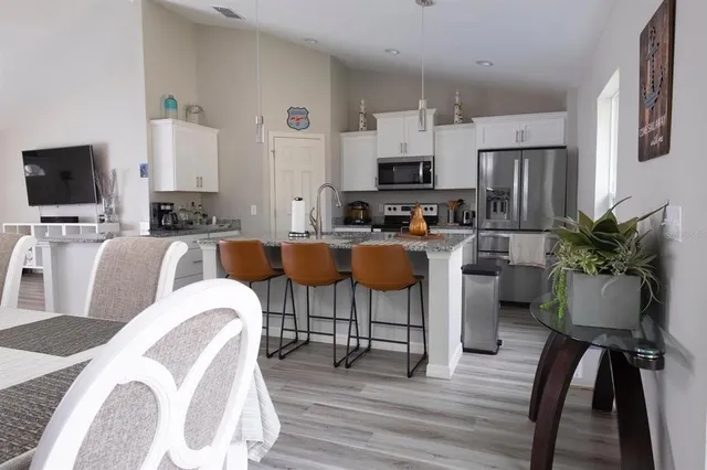 a living room with stainless steel appliances furniture a fireplace a flat screen tv and a kitchen view