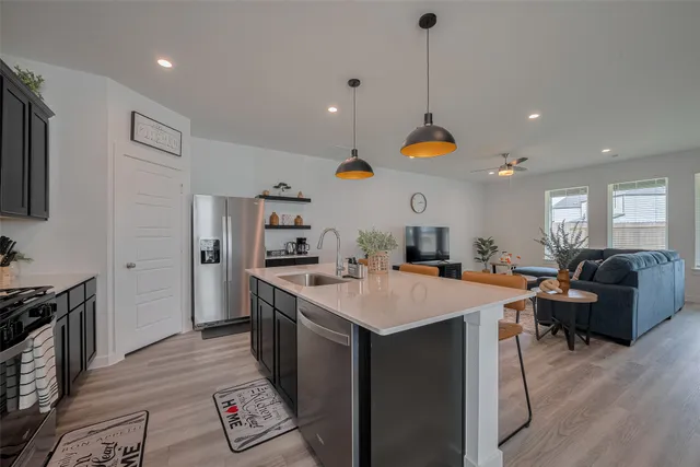 a large kitchen with stainless steel appliances a stove a sink a dining table chairs and couches with wooden floor