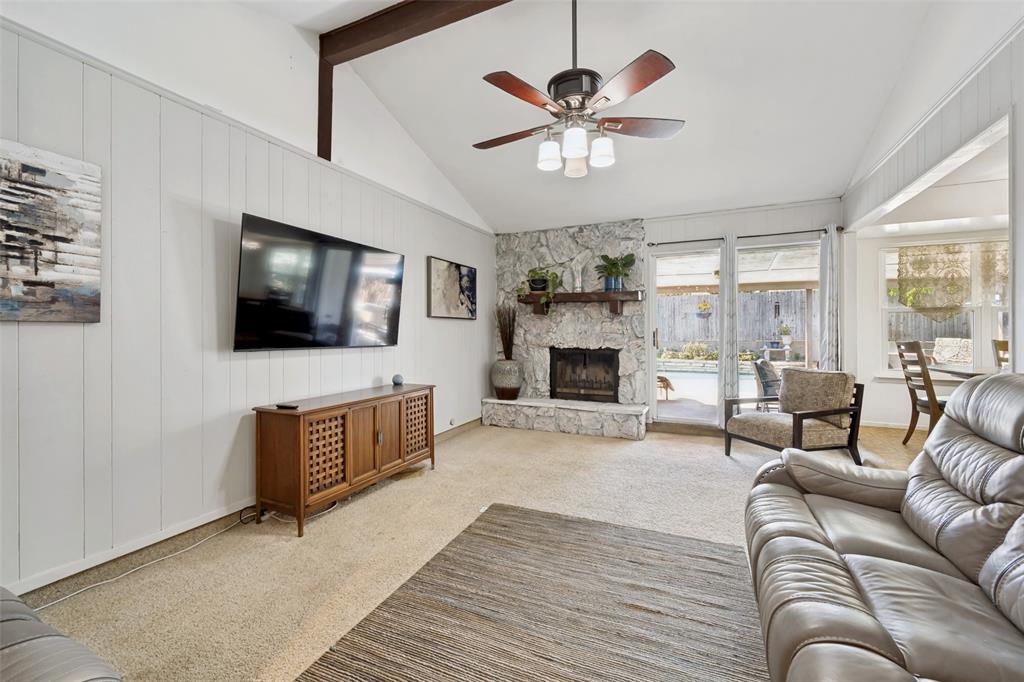 6484 Old Mill Circle Watauga, TX 76148 - Photo 4 of 25 Living room with carpet floors, ceiling fan, a stone fireplace, vaulted ceiling, and wood walls