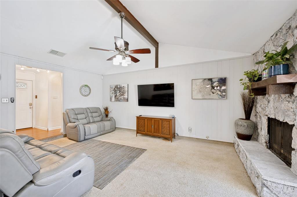 6484 Old Mill Circle Watauga, TX 76148 - Photo 8 of 25 Living room featuring light carpet, a stone fireplace, ceiling fan, and vaulted ceiling with beams