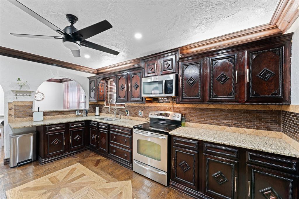 3318 San Marcus Avenue Dallas, TX 75228 - Photo 9 of 18 Kitchen featuring dark wood finish cabinets, crown molding, stainless steel appliances, parquet floors, and light stone counters