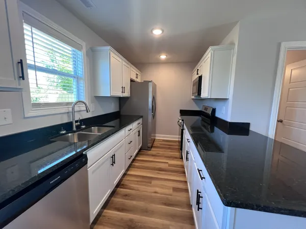 a large kitchen with granite countertop a sink and dishwasher a stove a refrigerator with wooden floor