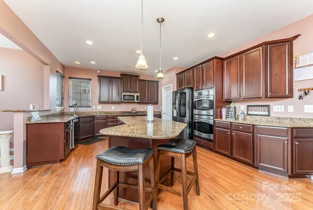 a kitchen with stainless steel appliances kitchen island granite countertop wooden cabinets a dining table and chairs
