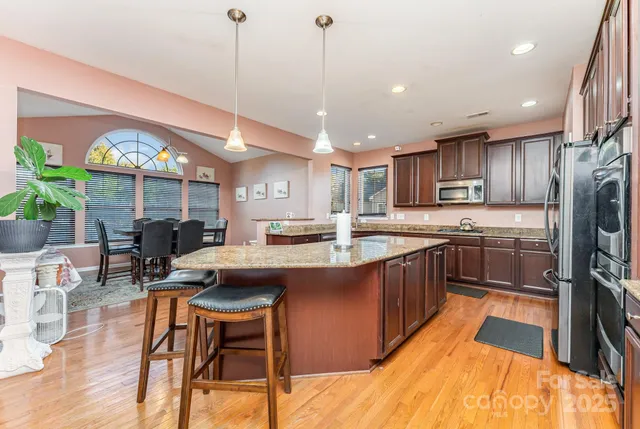 a kitchen with stainless steel appliances granite countertop a sink a stove a refrigerator cabinets and dining table