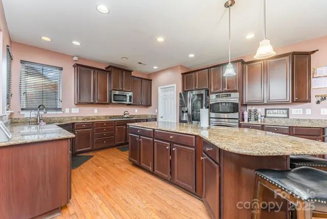 a large kitchen with kitchen island granite countertop wooden cabinets a stove a sink and a stainless steel appliances