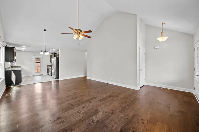 an empty room with wooden floor ceiling fan and kitchen view