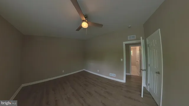 an empty room with wooden floor ceiling fan and windows