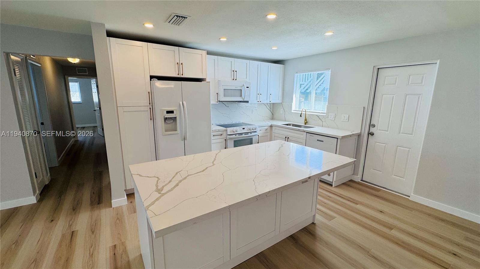 808 Northeast 2nd Street, Unit A Hallandale Beach, FL 33009 - Photo 3 of 11 a large kitchen with a refrigerator a sink a stove and white cabinets with wooden floor