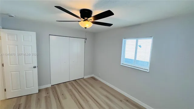 a view of an empty room with wooden floor and a ceiling fan