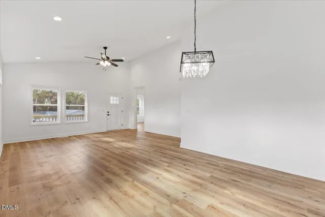 an empty room with wooden floor chandelier and windows