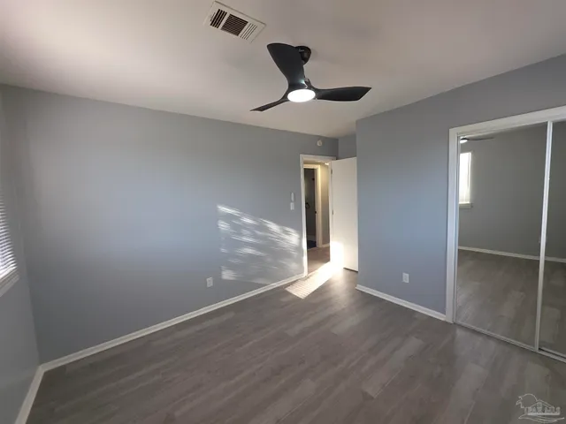 a view of an empty room with wooden floor and a ceiling fan