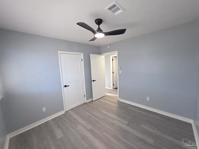a view of an empty room with wooden floor and a ceiling fan