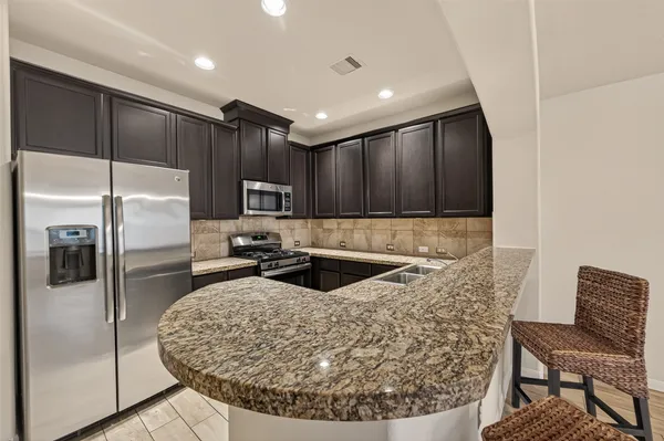 a kitchen with granite countertop a refrigerator and chairs