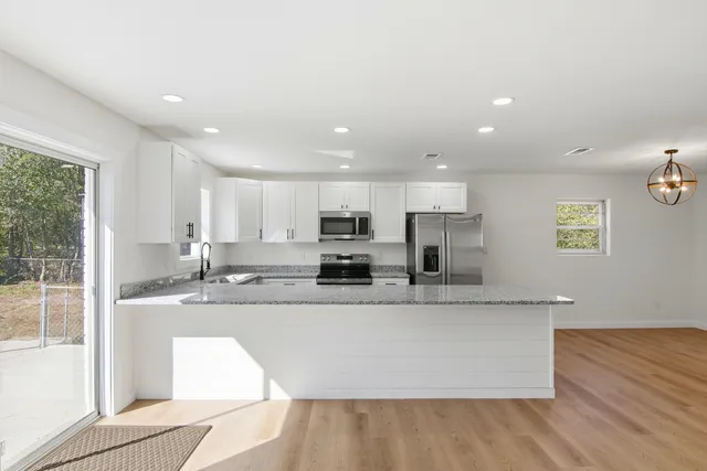 a large white kitchen with granite countertop a sink and dishwasher a stove with wooden floor