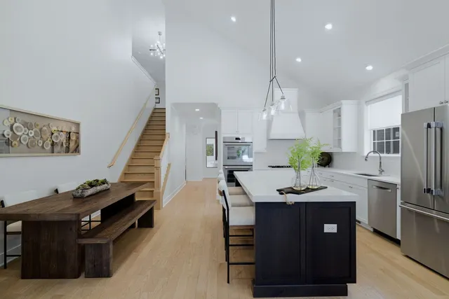 a kitchen with stainless steel appliances kitchen island granite countertop a refrigerator a sink dishwasher a stove and a dining table with wooden floor